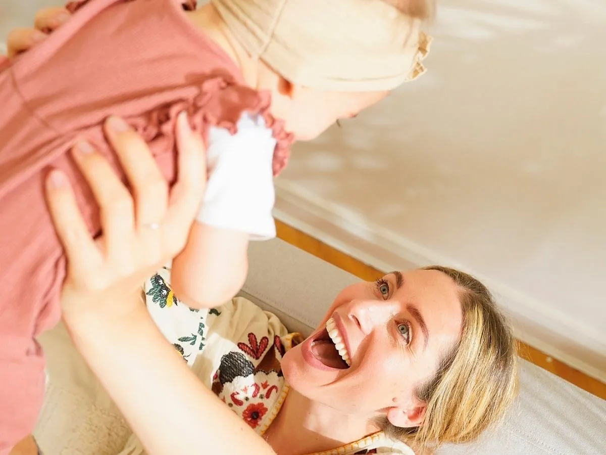 Jess Rose laughing as she lifts her baby daughter overhead