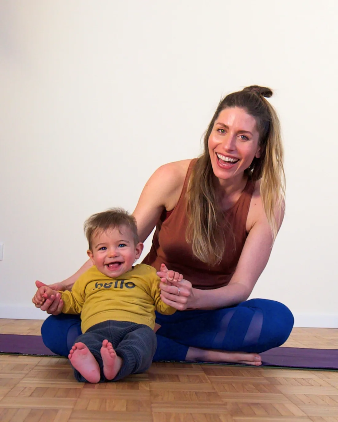 Jess Rose laughing on her mat with her baby son Dami in her lap