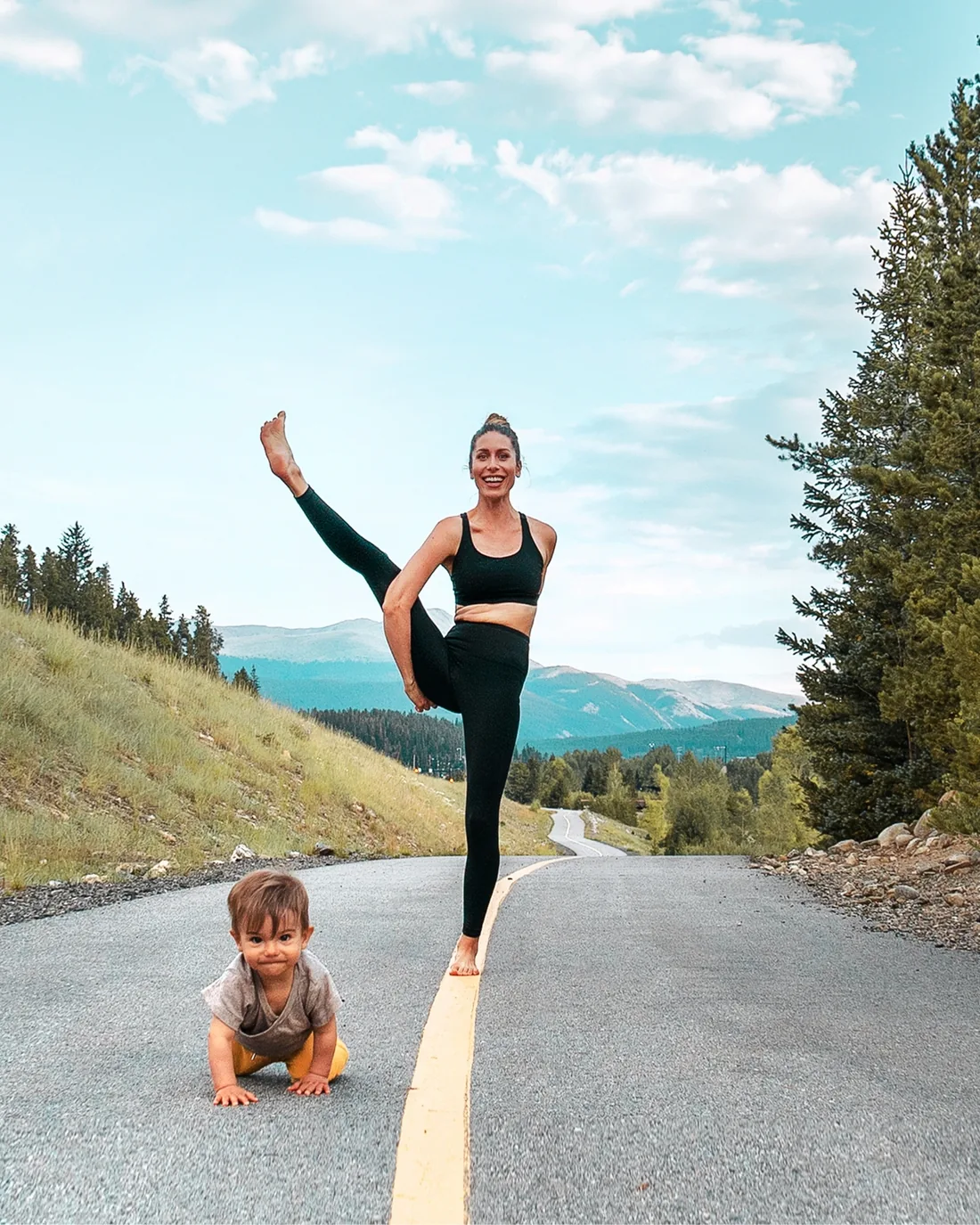 Jess Rose in a standing balance on a mountain road while her toddler son Dami crawls beside her